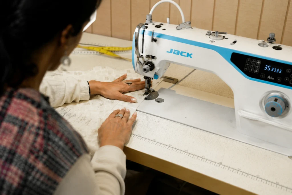 Seamstress operating a computerised industrial lockstitch sewing machine to stitch textured white fabric at Feel It Creation.