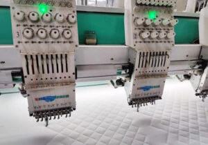 Multi-head computerized embroidery and quilting machine stitching diamond patterns on white padded fabric at Feel It Creation.