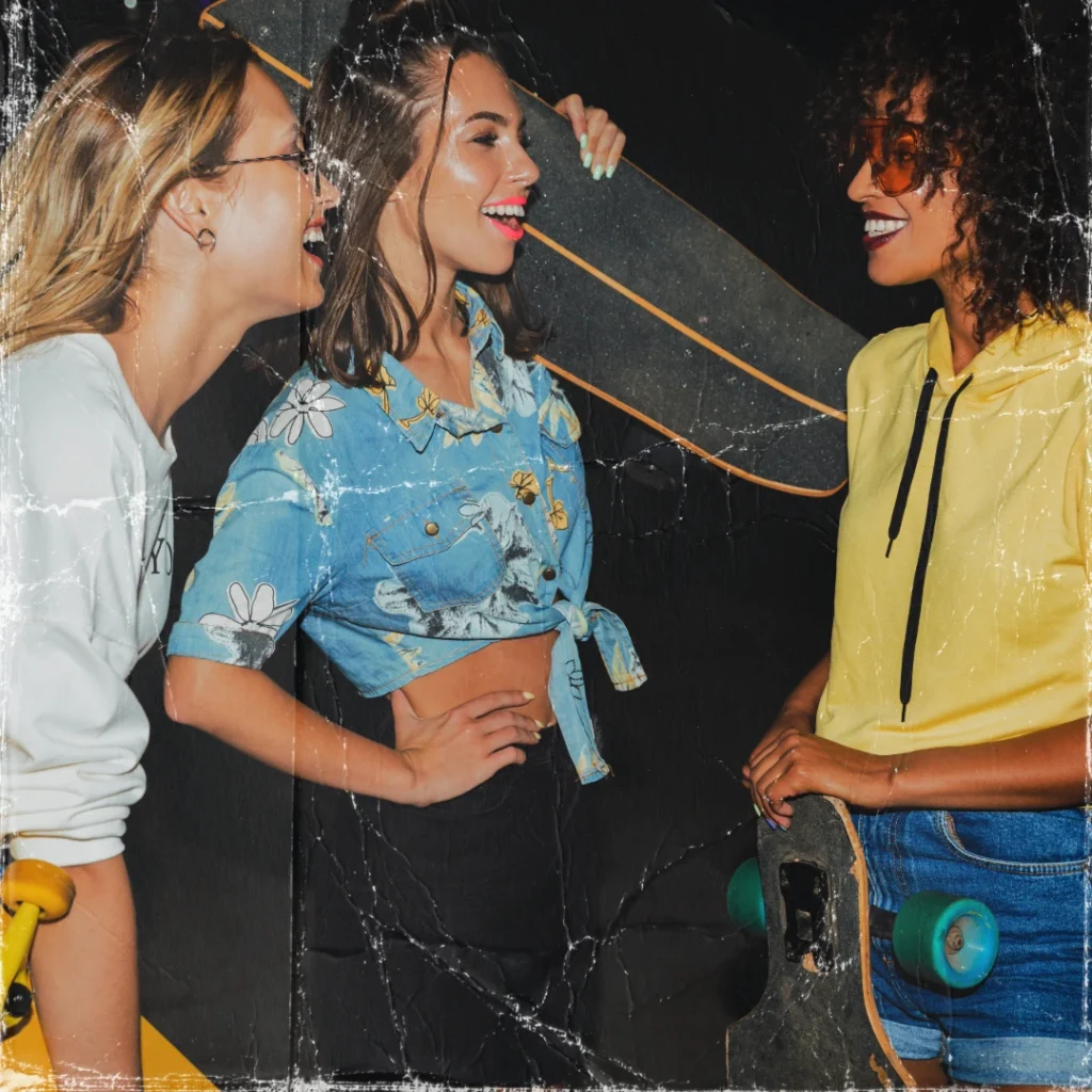 Three smiling young women with skateboards wearing custom streetwear, printed crop shirt, and hoodie manufactured by Feel It Creation.