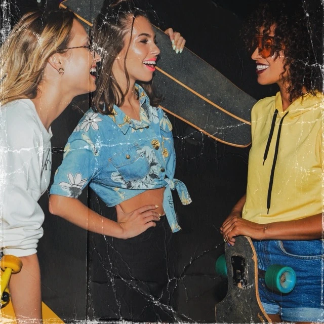 Three smiling young women with skateboards wearing custom streetwear, printed crop shirt, and hoodie manufactured by Feel It Creation.