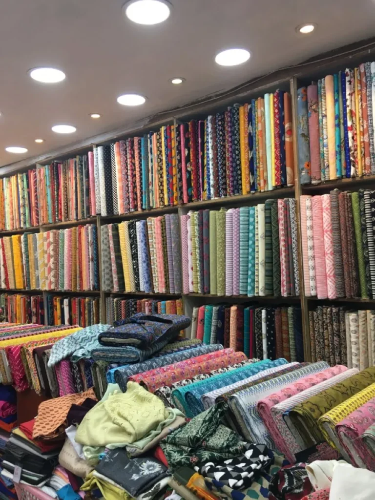 Shelves and display counters packed with colorful printed cotton and rayon fabric bolts at an Indian textile sourcing market